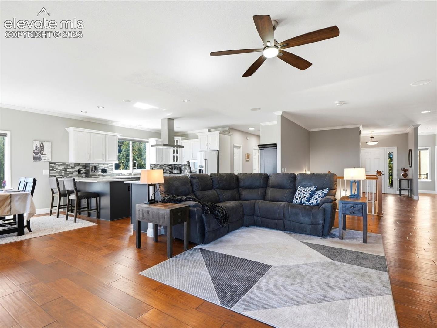Open-concept interior featuring wood-finish flooring, a kitchen island with bar seating, white cabinetry, a stainless steel range hood, and a ceiling fan