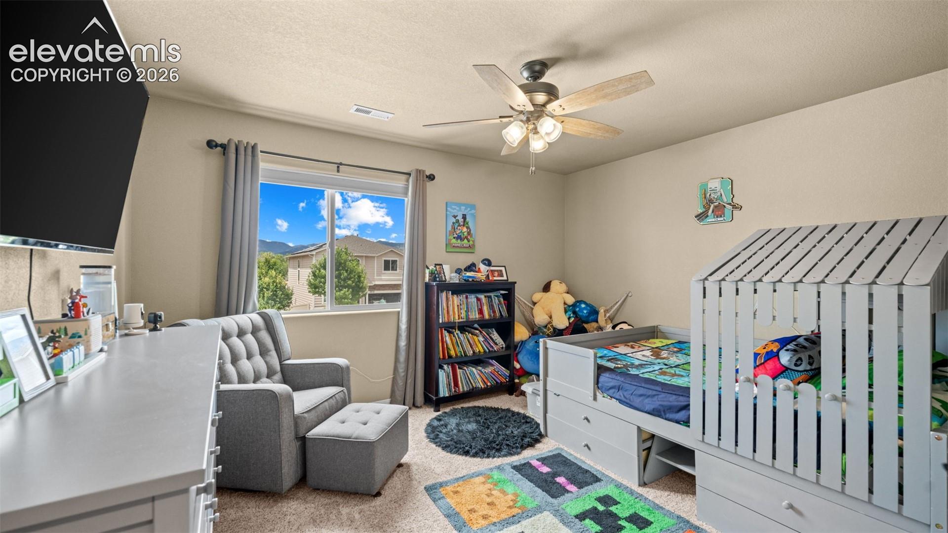 Carpeted room with a ceiling fan light fixture, window with drapes, and a built-in bookshelf