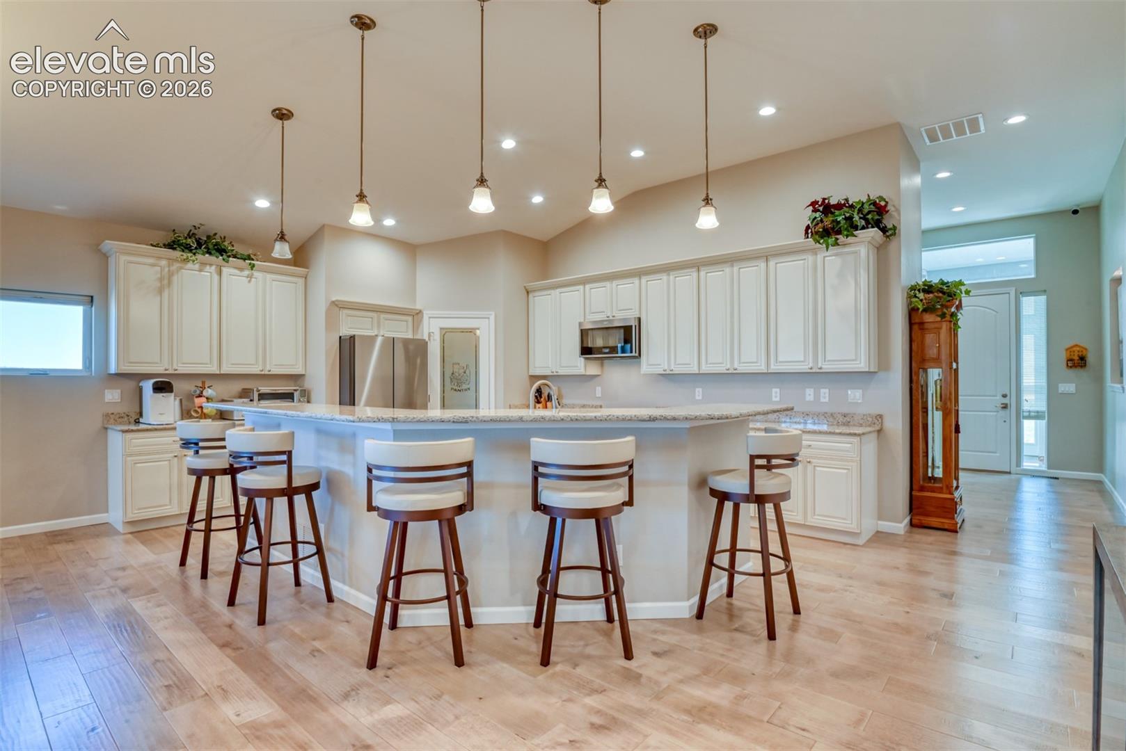 Kitchen featuring a curved breakfast bar, light wood-finish flooring, recessed lighting, pendant lighting, and white cabinetry.