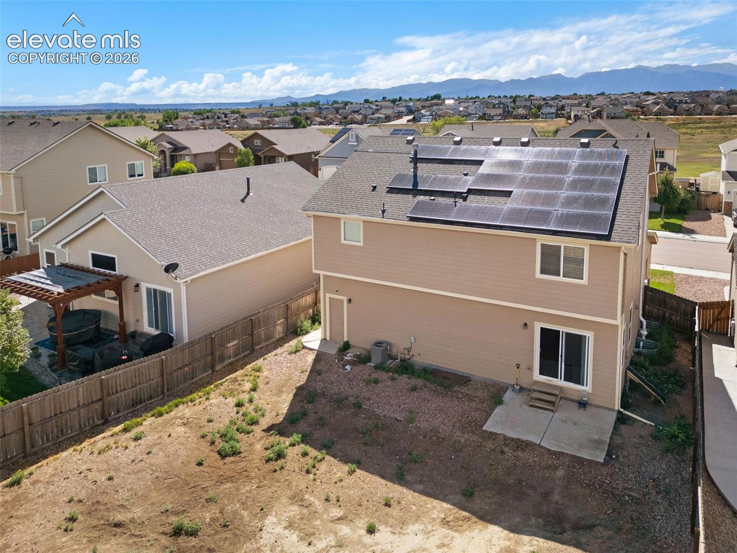 Two-story residence featuring a shingle roof with integrated solar panels, horizontal siding, sliding glass doors, and a concrete patio