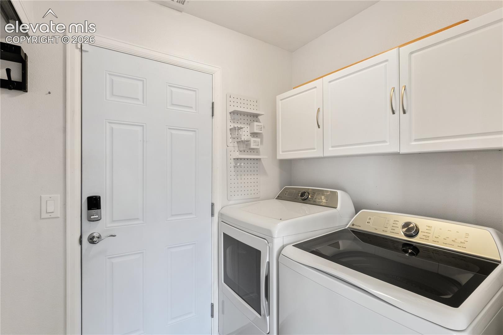 Utility space featuring white wall-mounted cabinetry, a solid-core paneled entry door with hardware, and a wall-mounted perforated organization panel