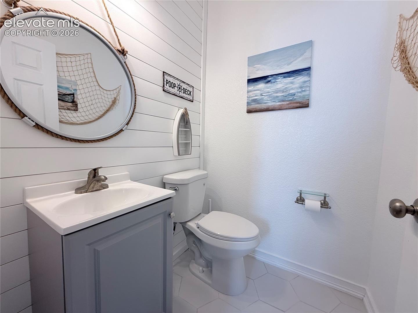 White shiplap accent wall, hexagonal tile flooring, vanity with integrated sink, contemporary faucet, and a toilet with a dual-flush mechanism