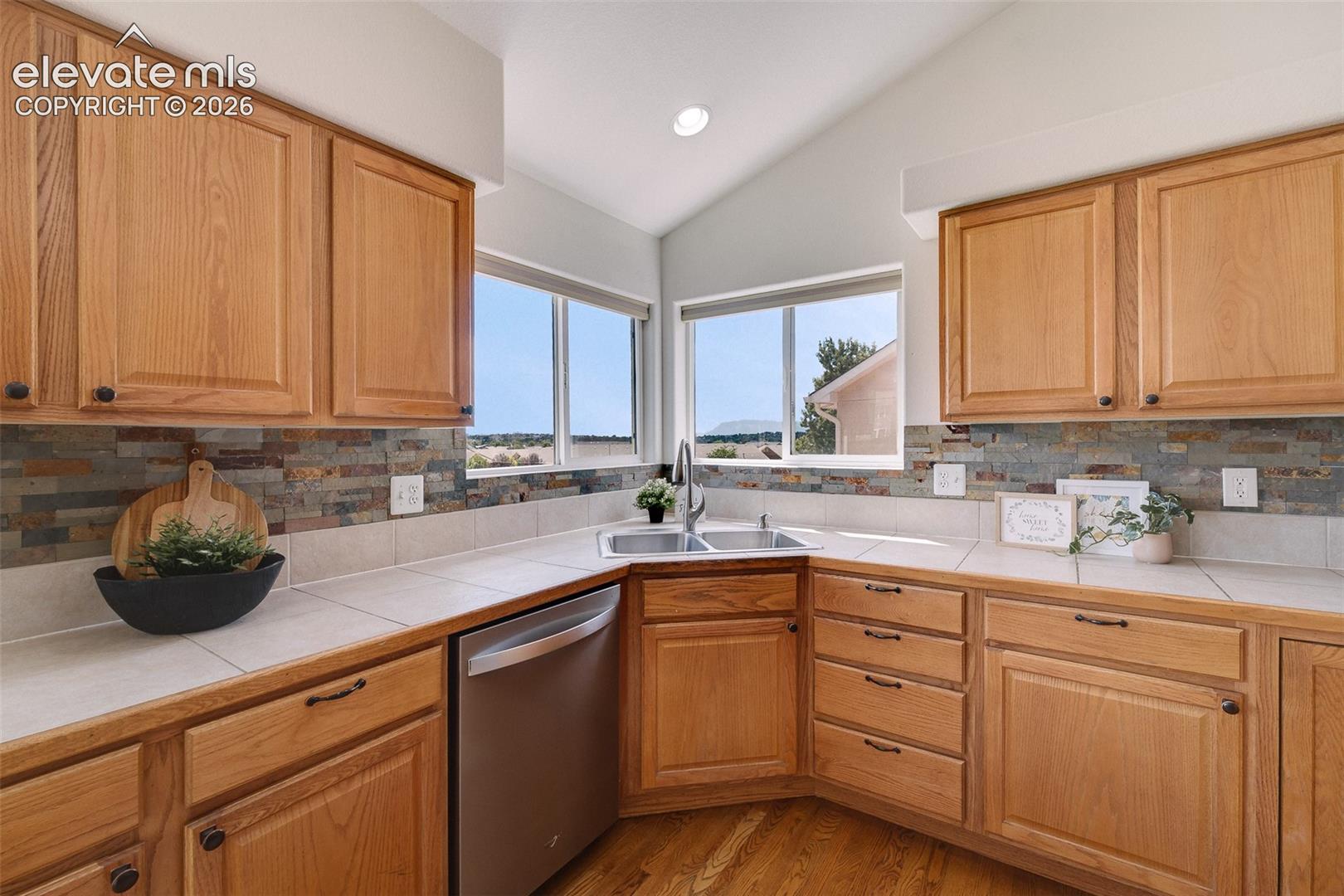 Kitchen featuring wood cabinetry, integrated stainless steel dishwasher, dual basin sink, and tile countertops