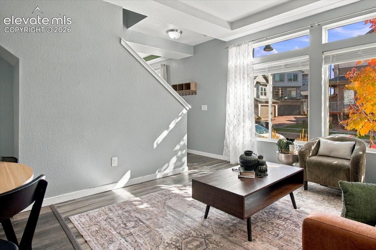 Recessed ceiling with an overhead light fixture, large windows with blinds, and wood-finish flooring