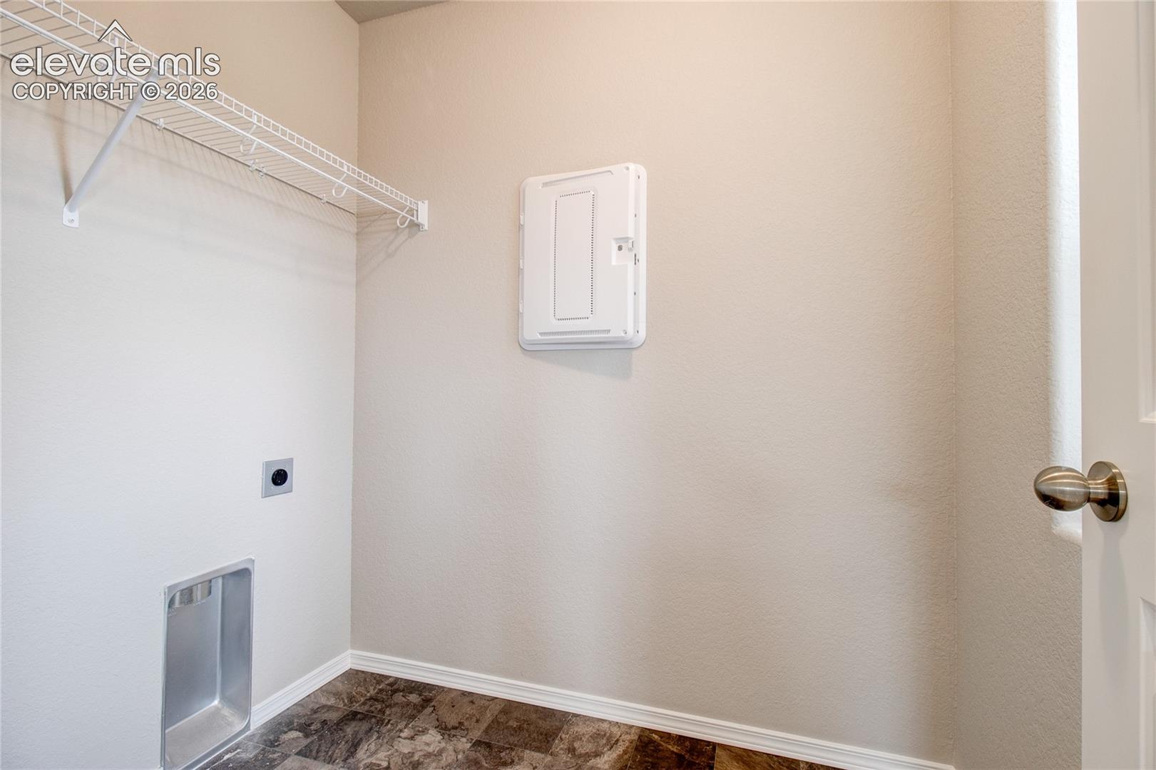 Utility space featuring tile flooring, metal wall-mounted shelving, and a recessed plumbing connection box