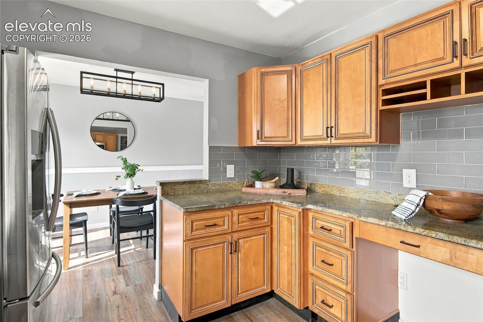 Kitchen featuring wood cabinetry, stone countertops, gray subway tile backsplash, and stainless steel refrigerator