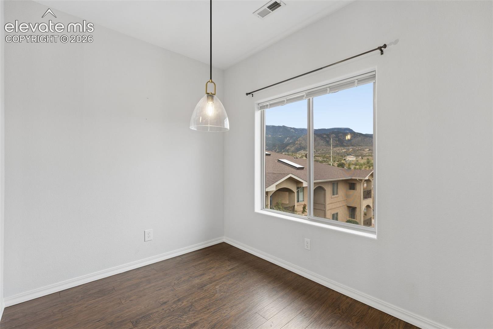 Room featuring wood-finish flooring, a metal-framed pendant light, and a large window showcasing a mountain backdrop