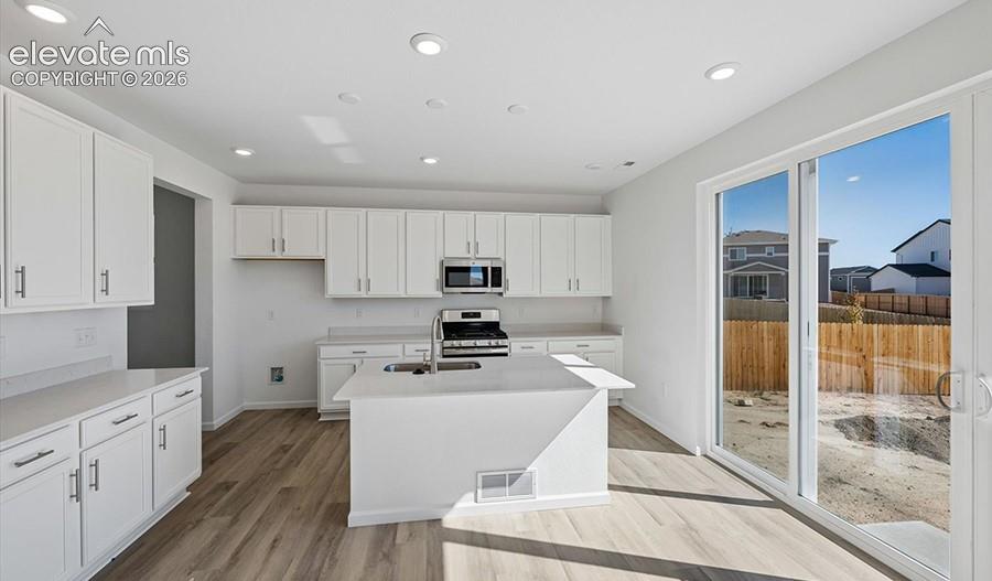 Kitchen featuring white cabinetry, center island with sink, stainless steel gas range, wood-finish flooring, and sliding glass doors