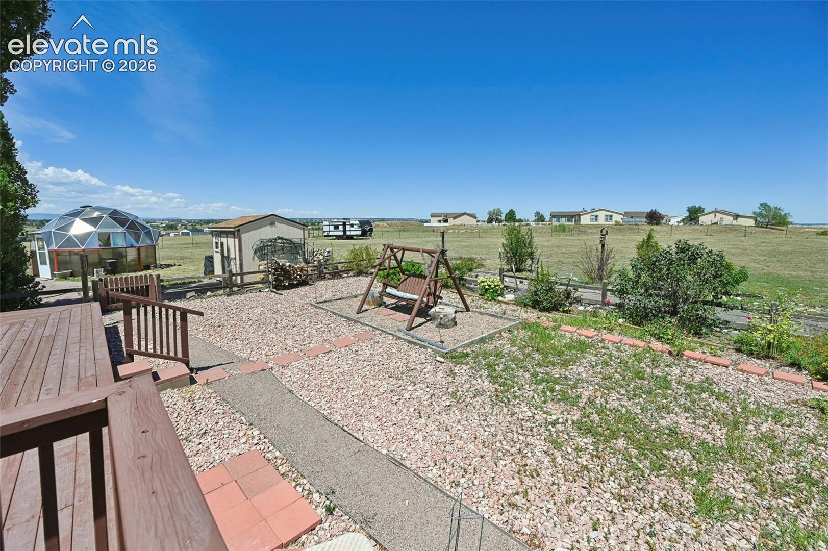 Outdoor wood-finish decking and railing, geodesic dome structure, gravel landscaping, and a wood-frame shed