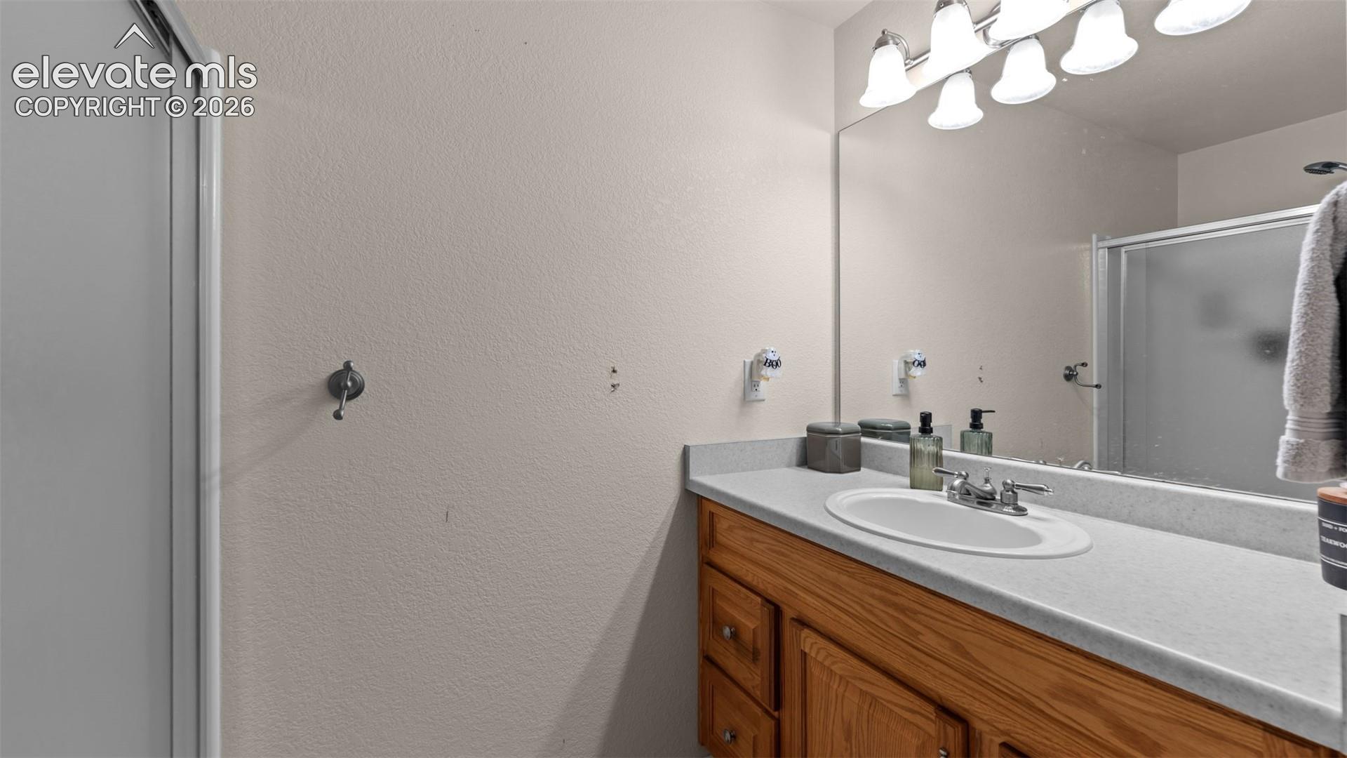 Vanity featuring a stone-composite countertop, integrated oval sink, multi-drawer wood cabinetry, full-width mirror, and multi-bulb vanity lighting