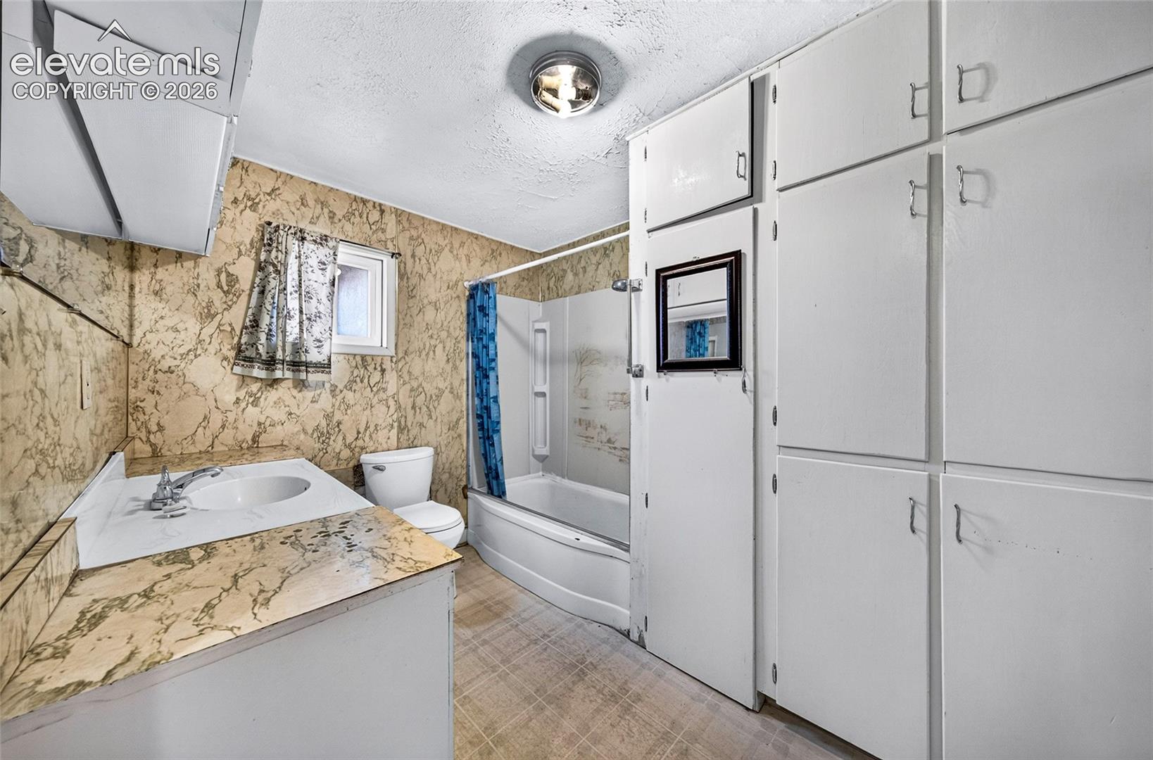 Built-in white cabinetry, full bathtub with shower, wall-mounted sink, and a light fixture