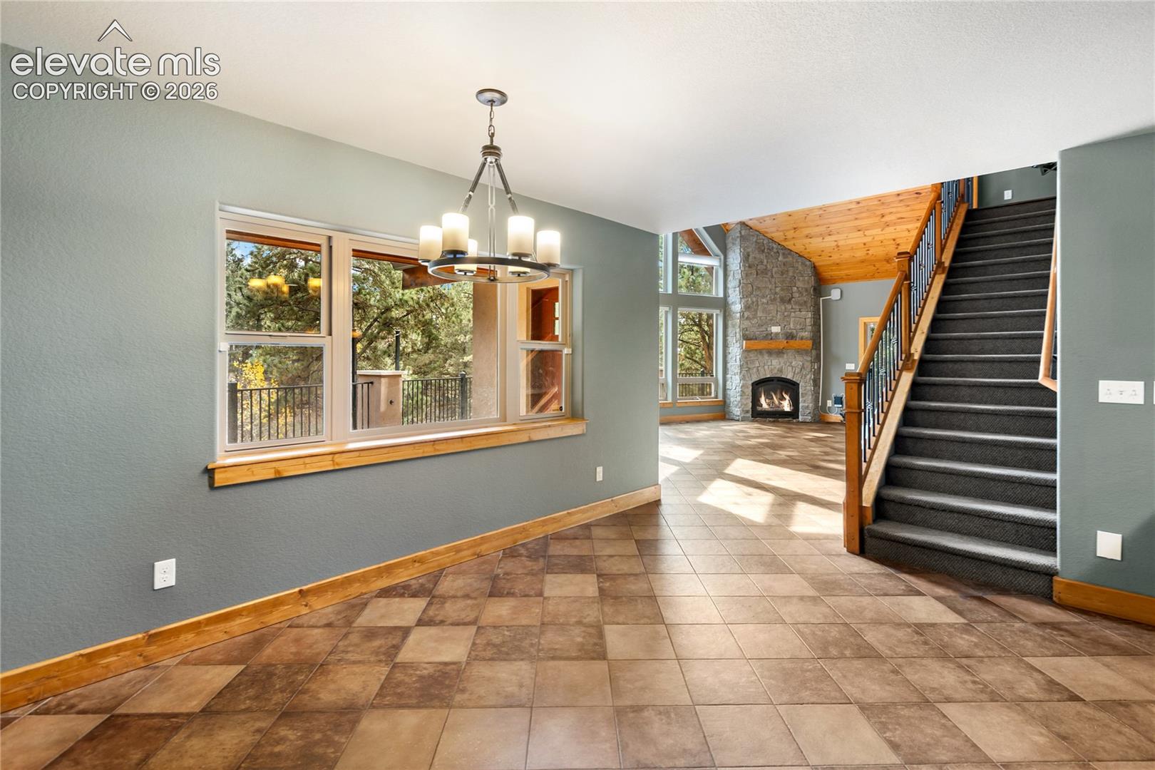 Interior space featuring diamond-patterned tile flooring, wood-trimmed windows, a multi-arm iron chandelier, and a wood-railed staircase with carpeted treads