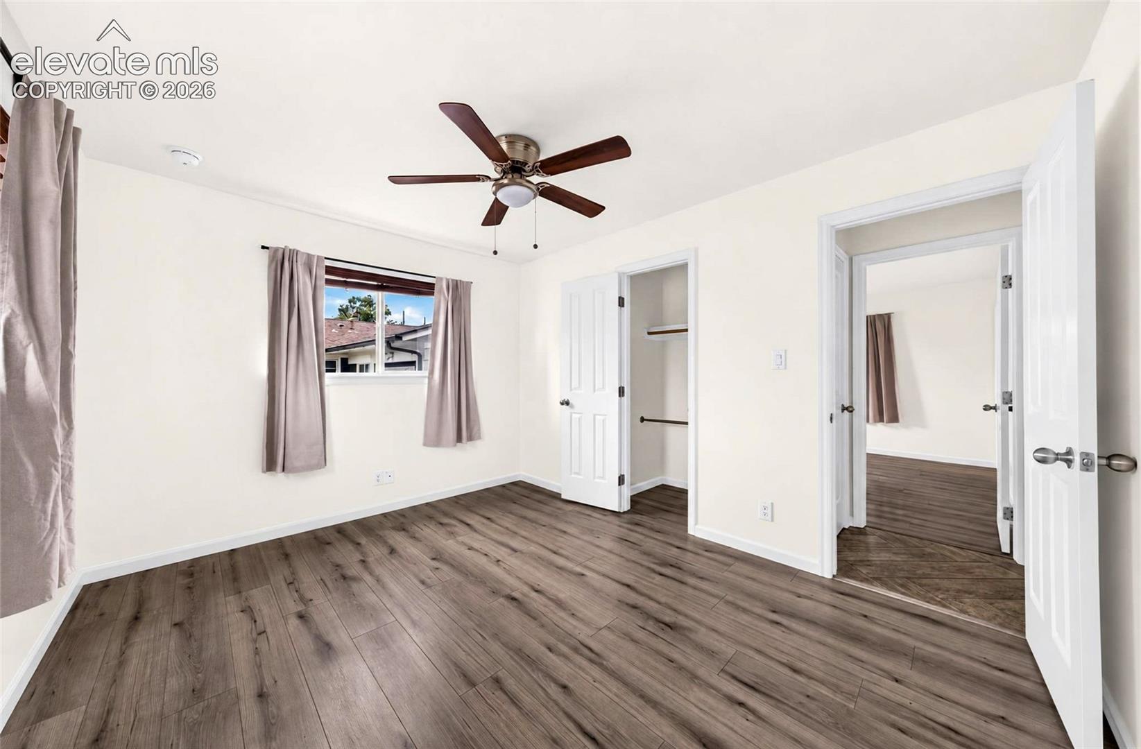 Room featuring wood-finish flooring, a ceiling fan with integrated lighting, a reach-in closet with built-in shelving, and a dual-pane window