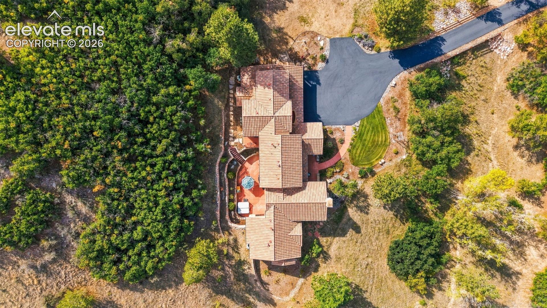 Property featuring a multi-level tile roof, extensive hardscaping, a large paved driveway, and varied landscaping with mature trees