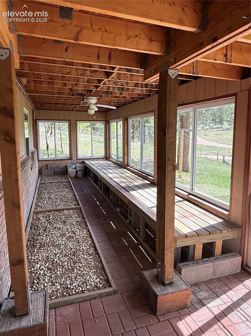 Sunroom featuring exposed wood beams, multiple large windows, brick paver flooring, a built-in wooden bench, and a ceiling fan