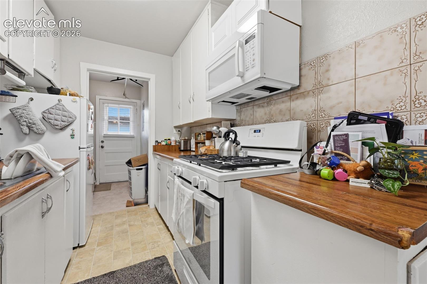 Galley kitchen with white cabinetry, wood-finish countertops, and patterned tile backsplash