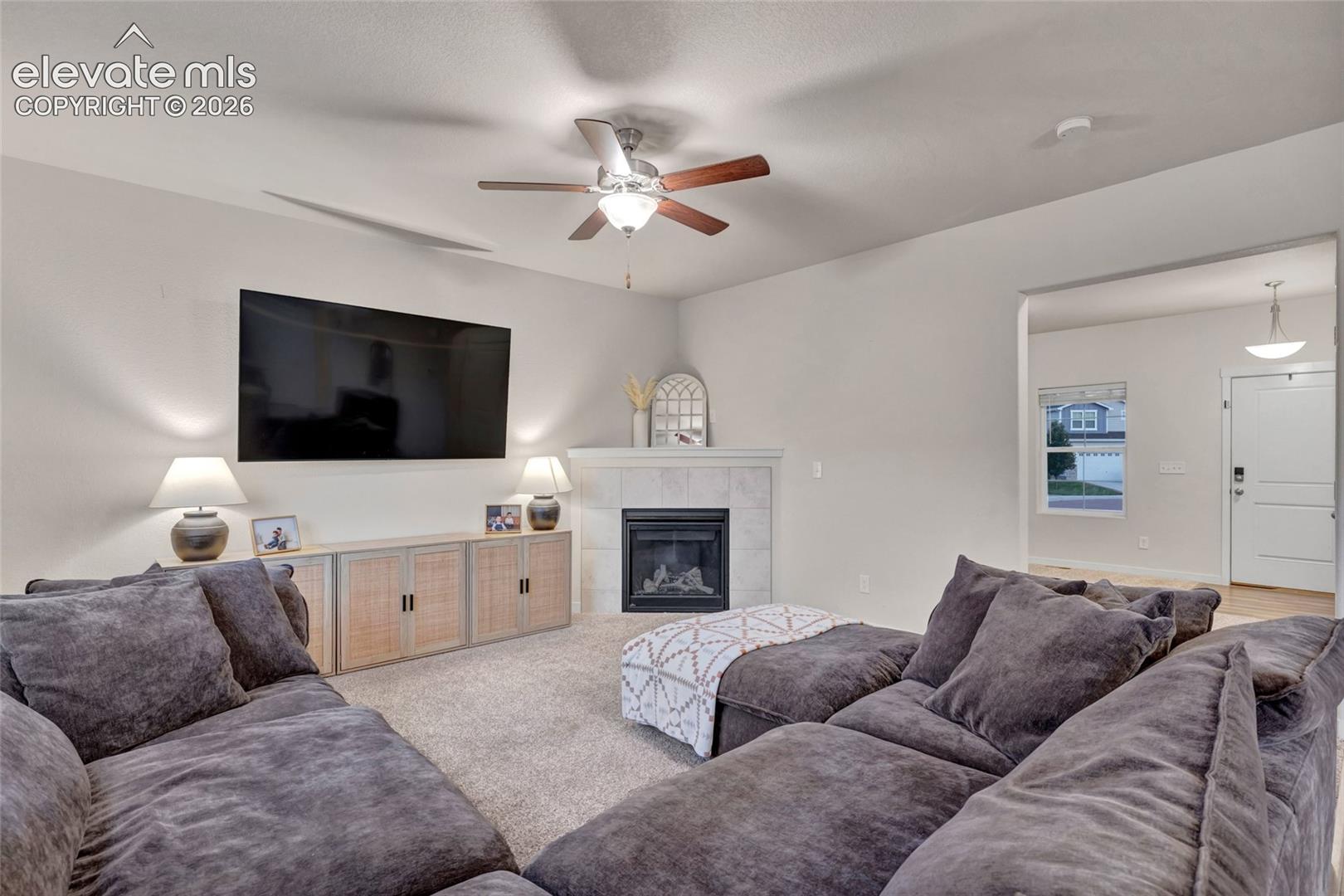 Spacious family room featuring a gas fireplace with white surround, built-in cabinetry with wood-finish doors, and a wall-mounted flat-screen television
