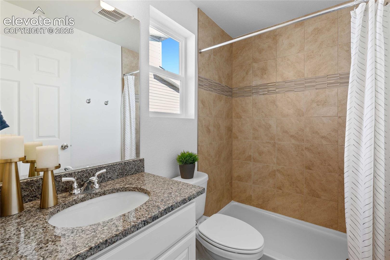 Bathroom featuring a granite-finish vanity countertop, single basin sink, and a tiled shower with an accent band
*photos of a model home*