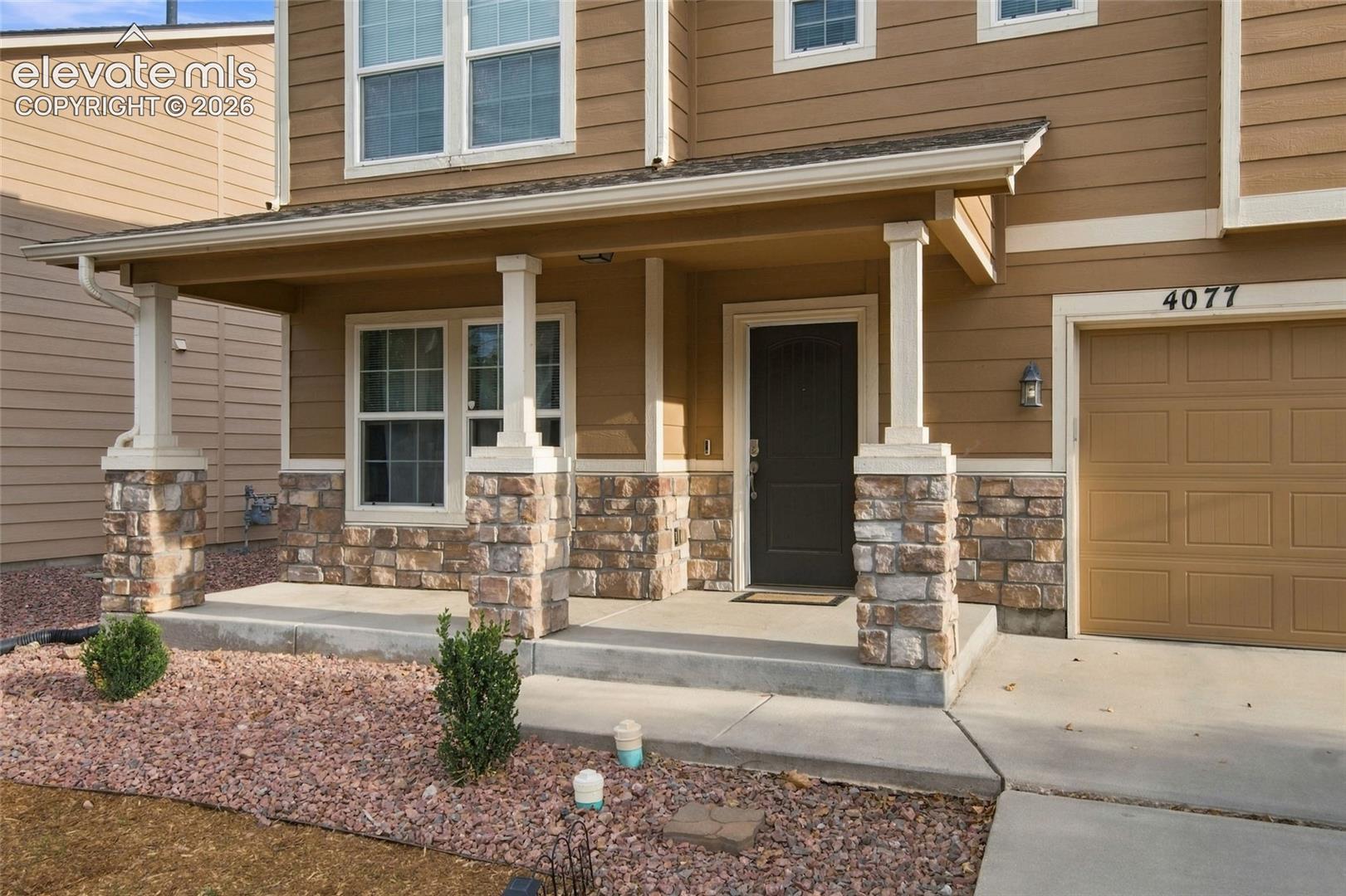 Exterior facade featuring horizontal siding, a covered front porch with stone-veneer column bases, multi-pane windows, and a multi-panel garage door