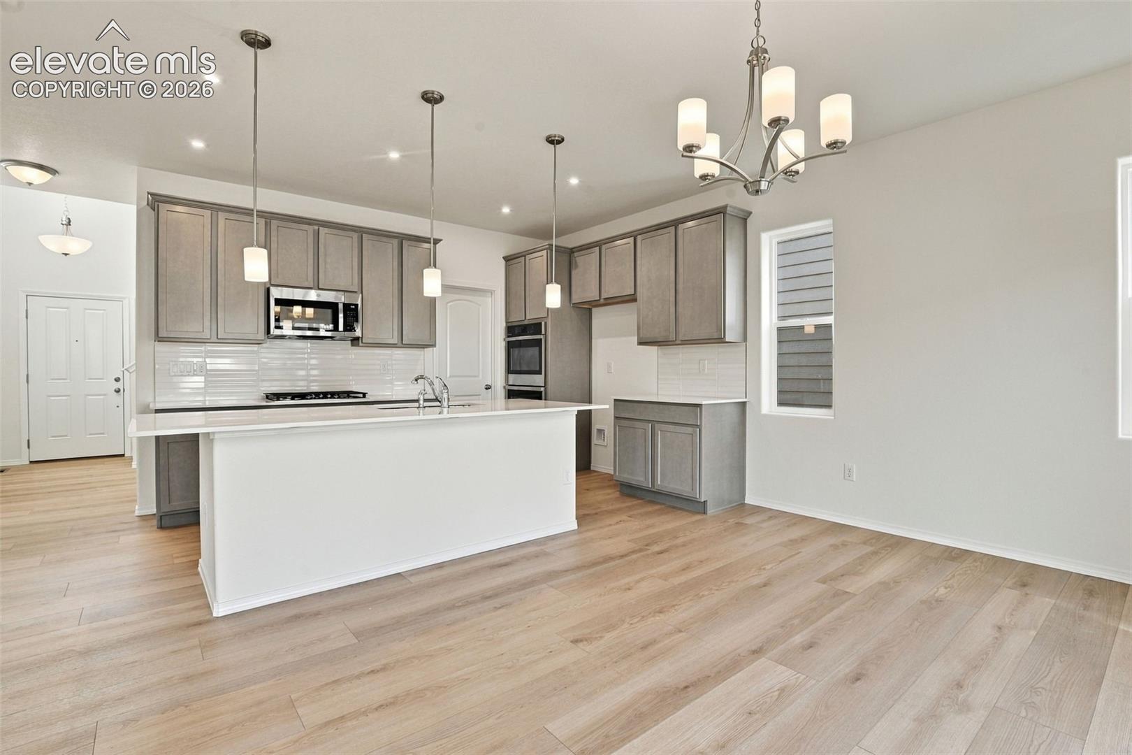 Kitchen featuring a central island with a stone-finish countertop, shaker-style cabinetry, recessed lighting, pendant fixtures, and wood-finish flooring