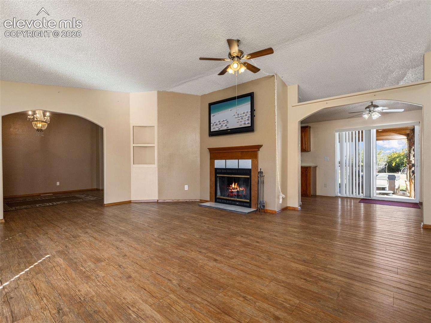 Living area featuring wood-finish flooring, a fireplace with a wood mantel, dual arched wall openings, and ceiling fan lighting fixtures