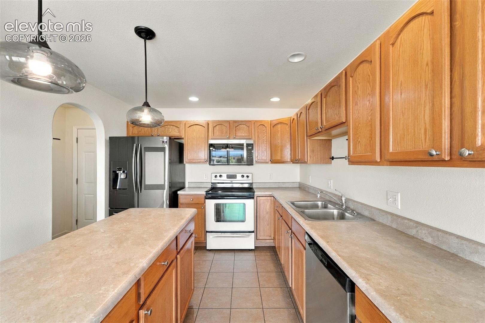 Kitchen featuring wood cabinetry, stone-finish countertops, ceramic tile flooring, dual-basin stainless steel sink, and glass pendant lighting