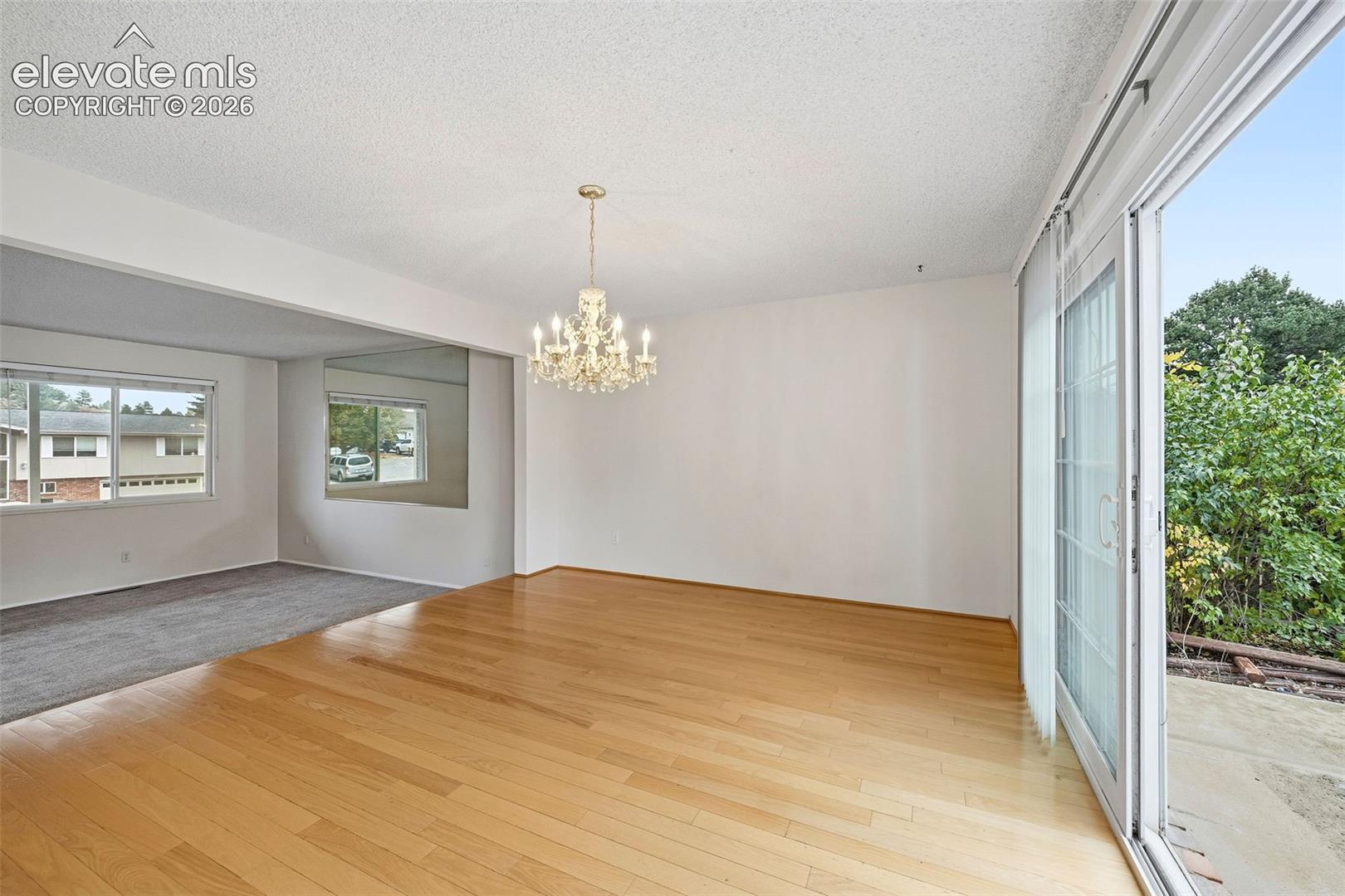 Light-filled interior featuring wood-finish flooring, a multi-arm chandelier, large wall-to-wall mirror, and sliding glass doors with access to an exterior concrete patio