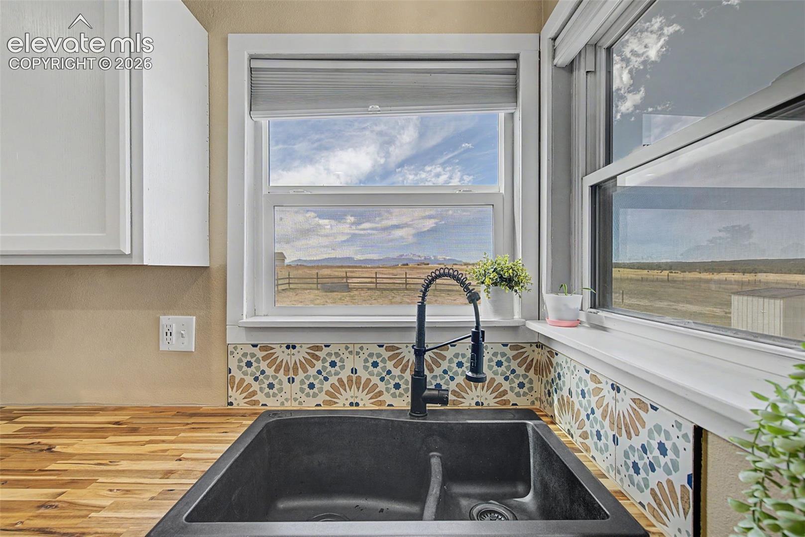 Double-basin composite sink featuring a matte black pull-down faucet, butcher block countertop, patterned decorative tile backsplash, and dual windows with mountain scenery