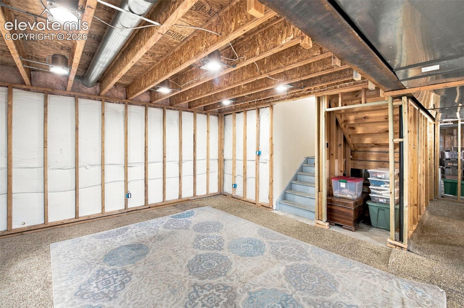 Unfinished lower level featuring exposed wood joist ceilings, framed wall construction with insulation, recessed lighting, and wooden staircase
