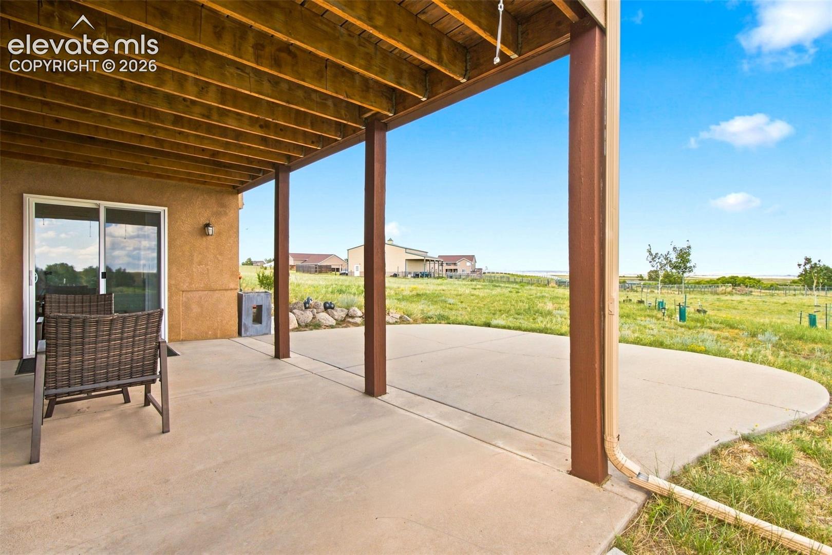 Expansive covered patio with wood-beam ceiling and structural steel supports overlooking open acreage