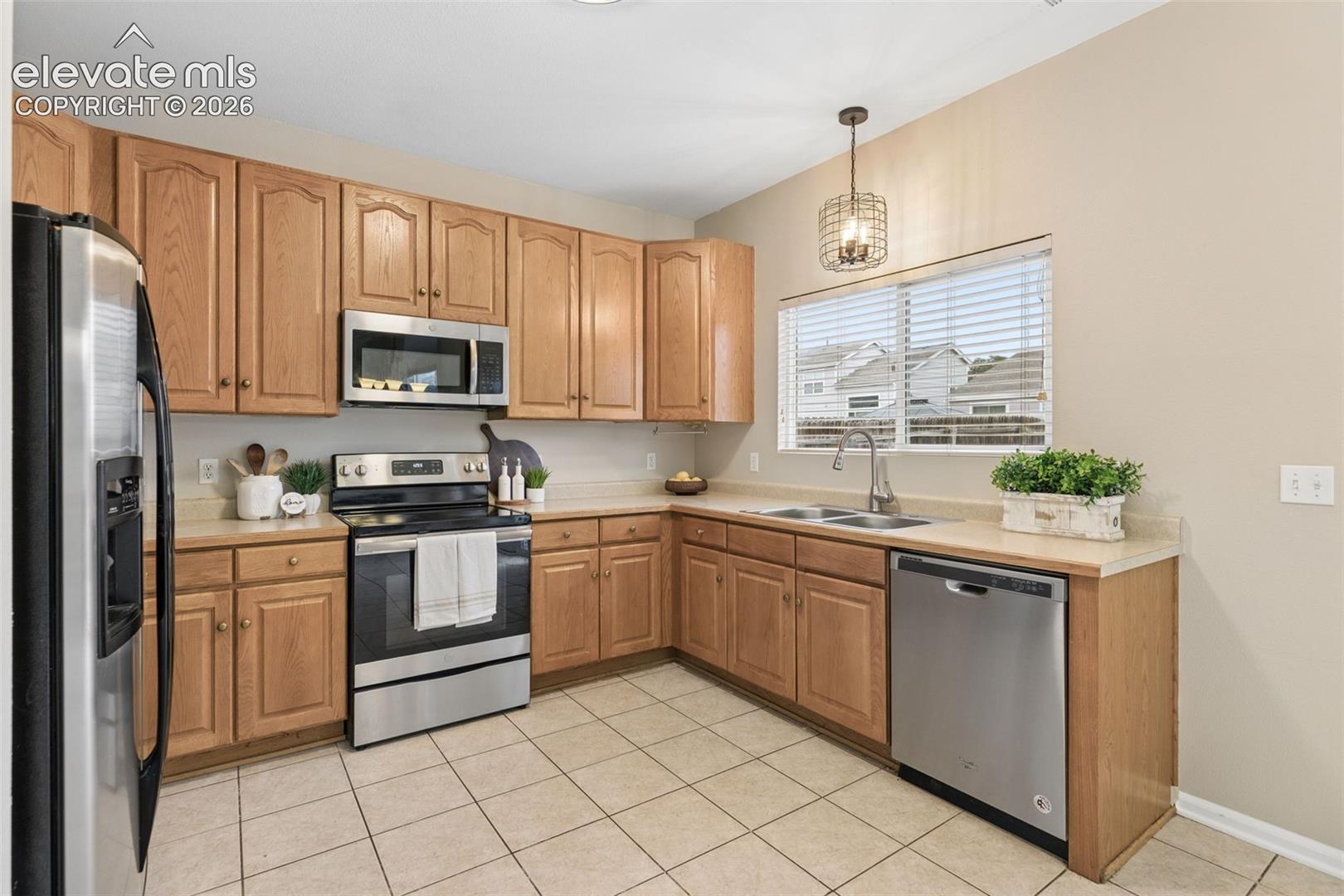 Kitchen featuring wood cabinetry, stainless steel appliances, tile flooring, laminate countertops, and a pendant light fixture