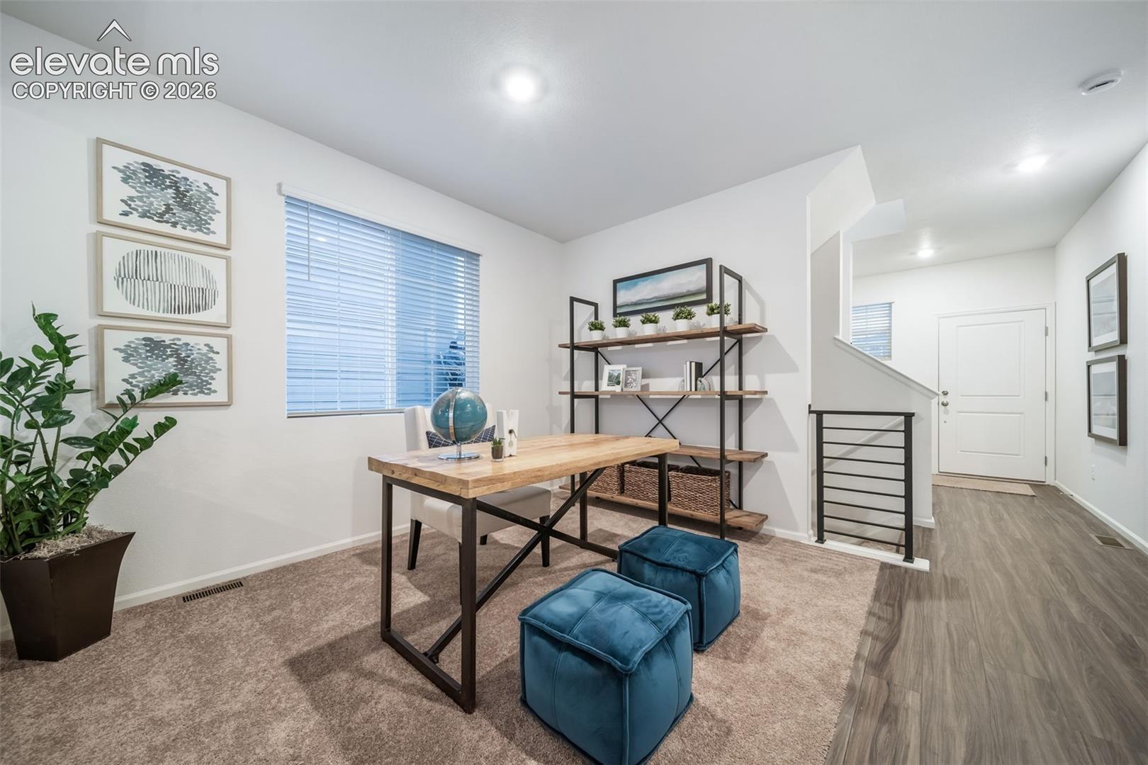 Carpeted room with a window featuring blinds, a built-in open-shelf unit, and wood-finish flooring extending into the hall
*photos of a model home*