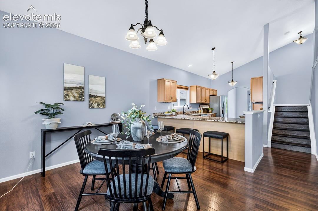 Vaulted ceilings, wood-finish flooring, breakfast bar with stone countertop, multi-arm chandelier lighting, and staircase with dark-finished treads