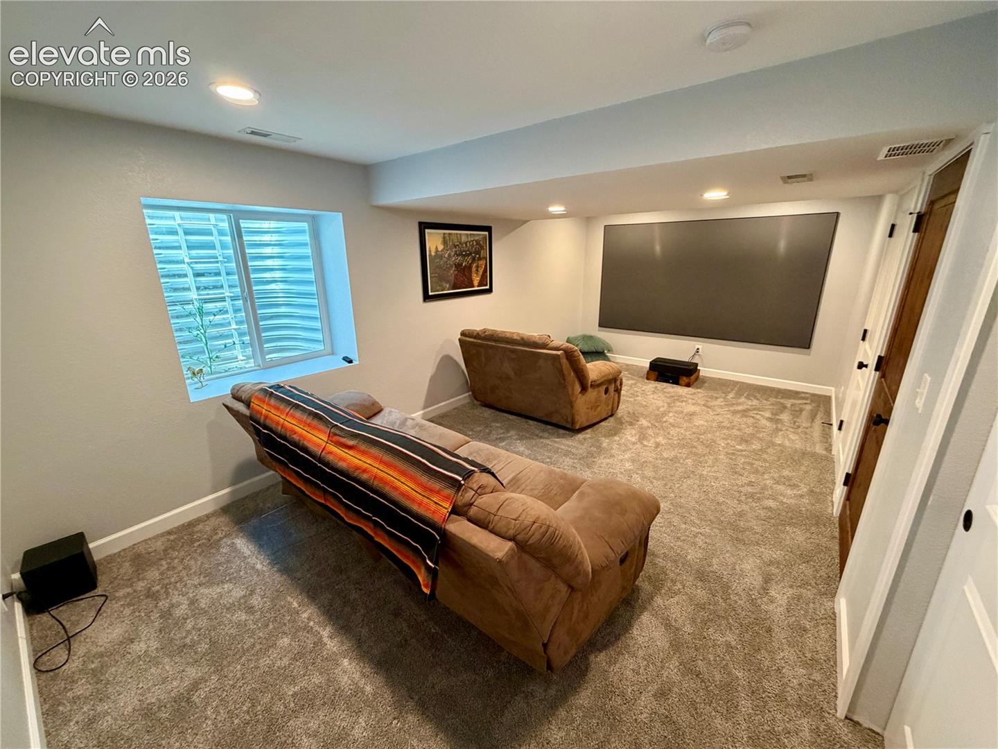 Basement bedroom or media room featuring a large projection screen, recessed lighting, and soft gray carpeting. Th