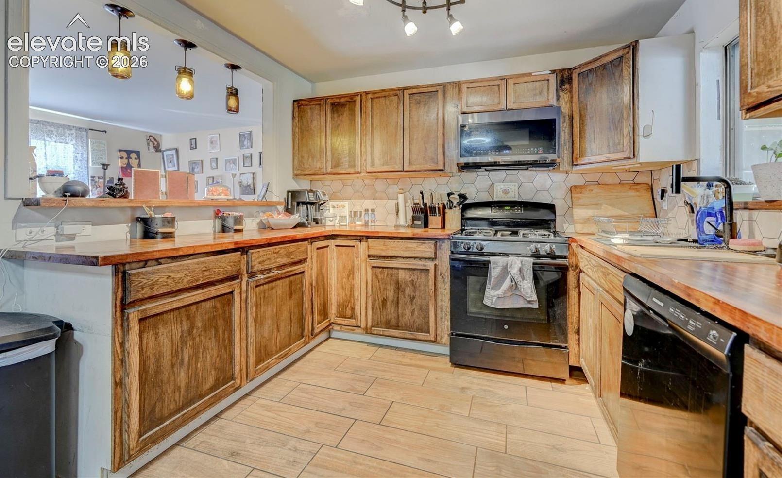 Kitchen featuring wood cabinetry, butcher block countertops, hexagon-tile backsplash, wood-finish tile flooring, and three pendant lights