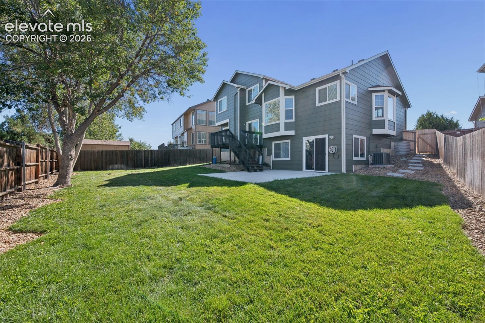 Rear exterior featuring horizontal lap siding, an elevated deck with stairs, a concrete patio, and a fenced backyard