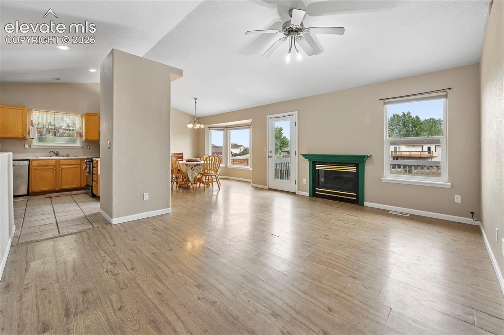 Open-concept living space featuring wood-finish flooring, a ceiling fan with integrated lighting, and a green mantel fireplace