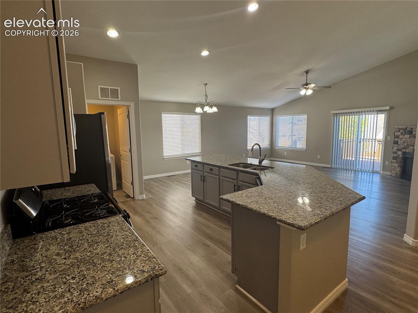 Kitchen featuring a stone-topped island, wood-finish flooring, vaulted ceilings, recessed lighting, and a stone-accented fireplace