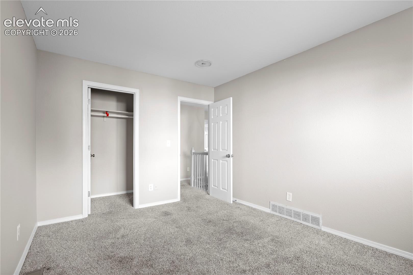 Neutral wall tones, wall-to-wall carpeting, and a built-in closet with an integrated shelf and rod
