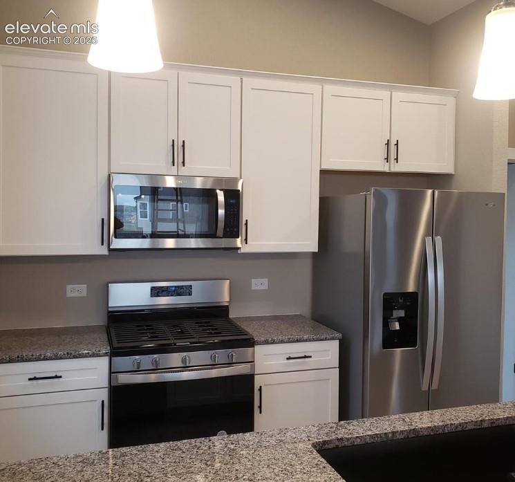 Kitchen featuring white shaker-style cabinetry, stone countertops, stainless steel appliances, and pendant lighting
