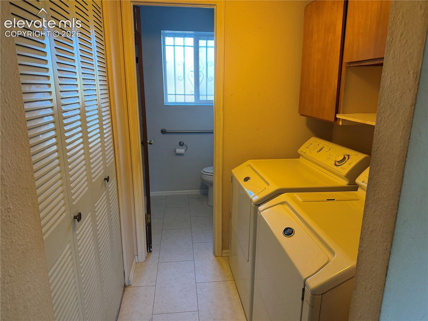 Utility area in lower level featuring tile flooring, bi-fold louvered closet doors, and wall-mounted wooden cabinetry