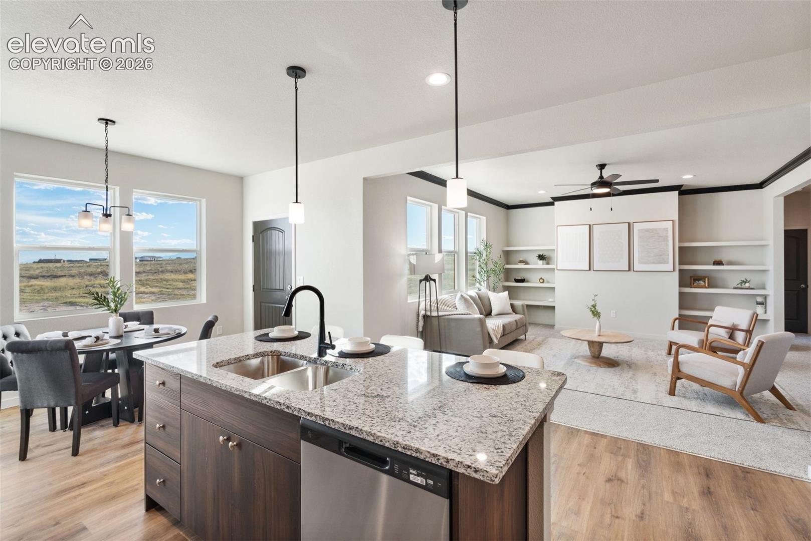Open-concept living space featuring a kitchen island with granite countertops, stainless steel appliances, wood-finish flooring, built-in shelving, and multiple windows