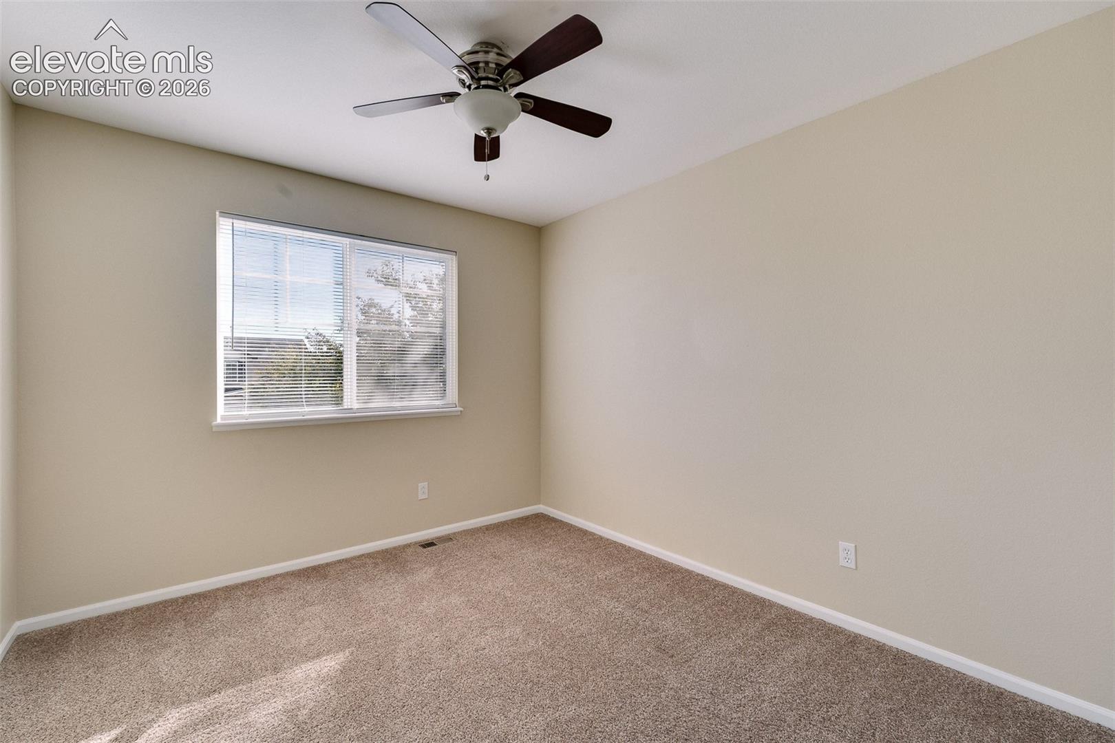 Neutral-toned interior space featuring wall-to-wall carpeting, a multi-blade ceiling fan with integrated lighting, and a single-pane sliding window
