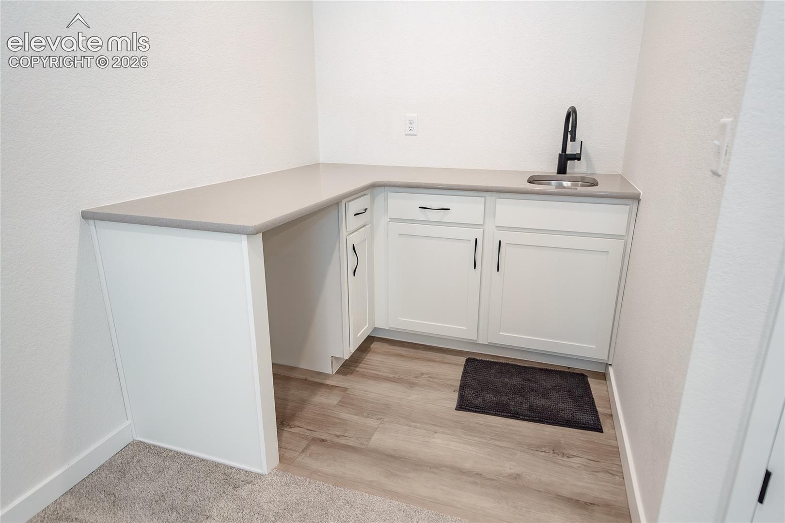 Built-in cabinetry featuring white shaker-style doors, matte black hardware, a solid-surface countertop, an integrated sink, and a matte black gooseneck faucet