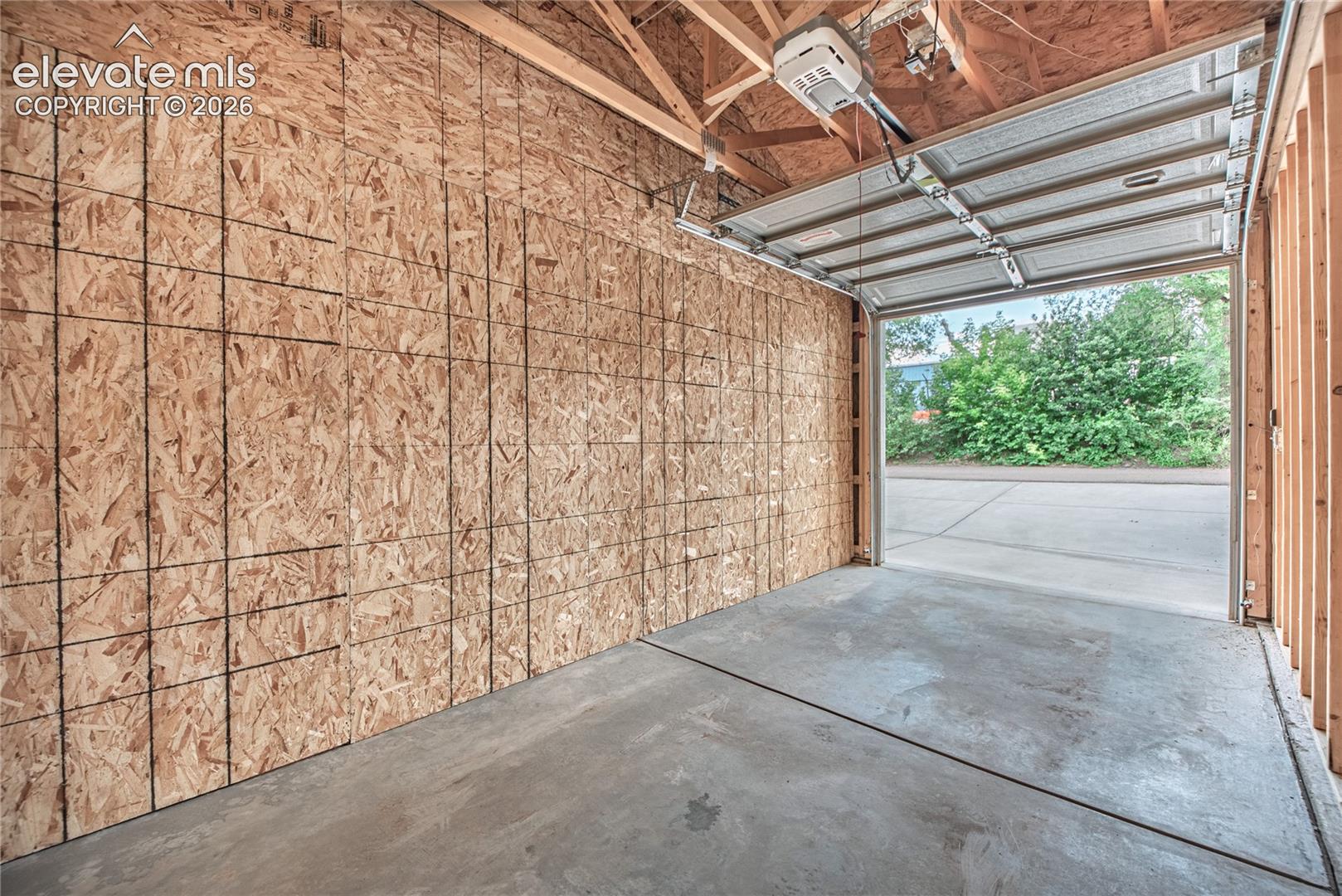 Garage space featuring an automatic overhead door, exposed wood framing, oriented strand board walls, and a concrete floor
