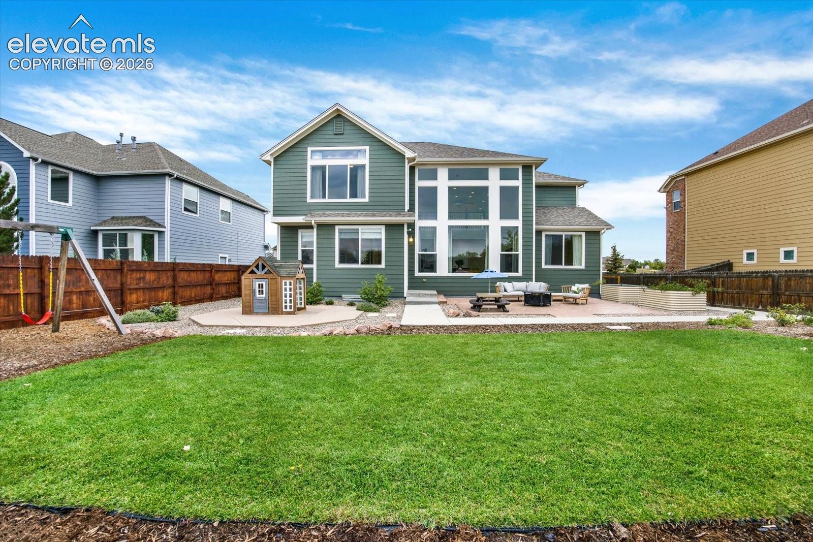 Rear exterior featuring horizontal lap siding, multi-story grid windows, a concrete patio, and a wood privacy fence
