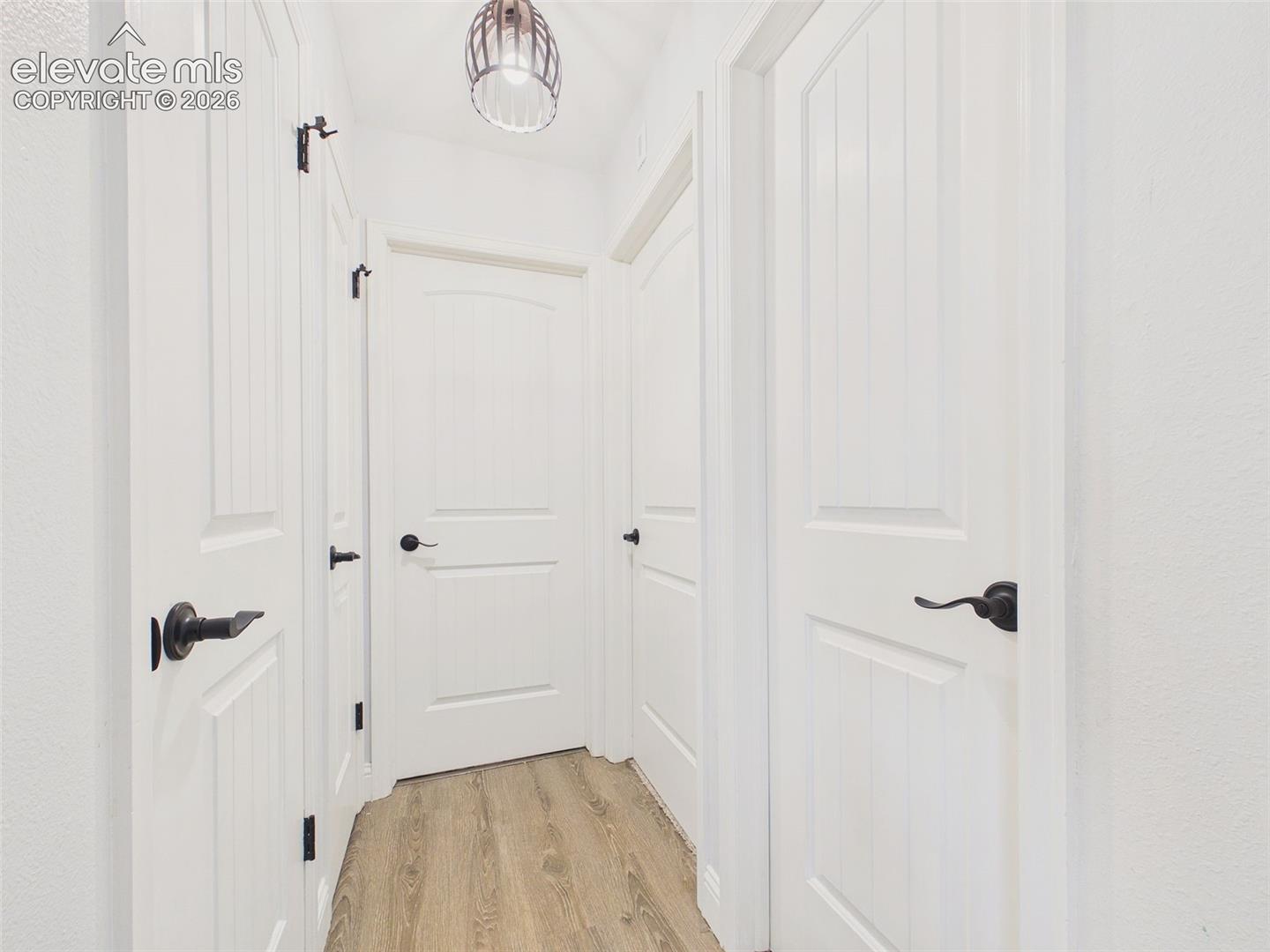 Bright interior hallway showcases updated paneled doors with contrasting dark hardware and wood-look flooring for a clean, cohesive finish.