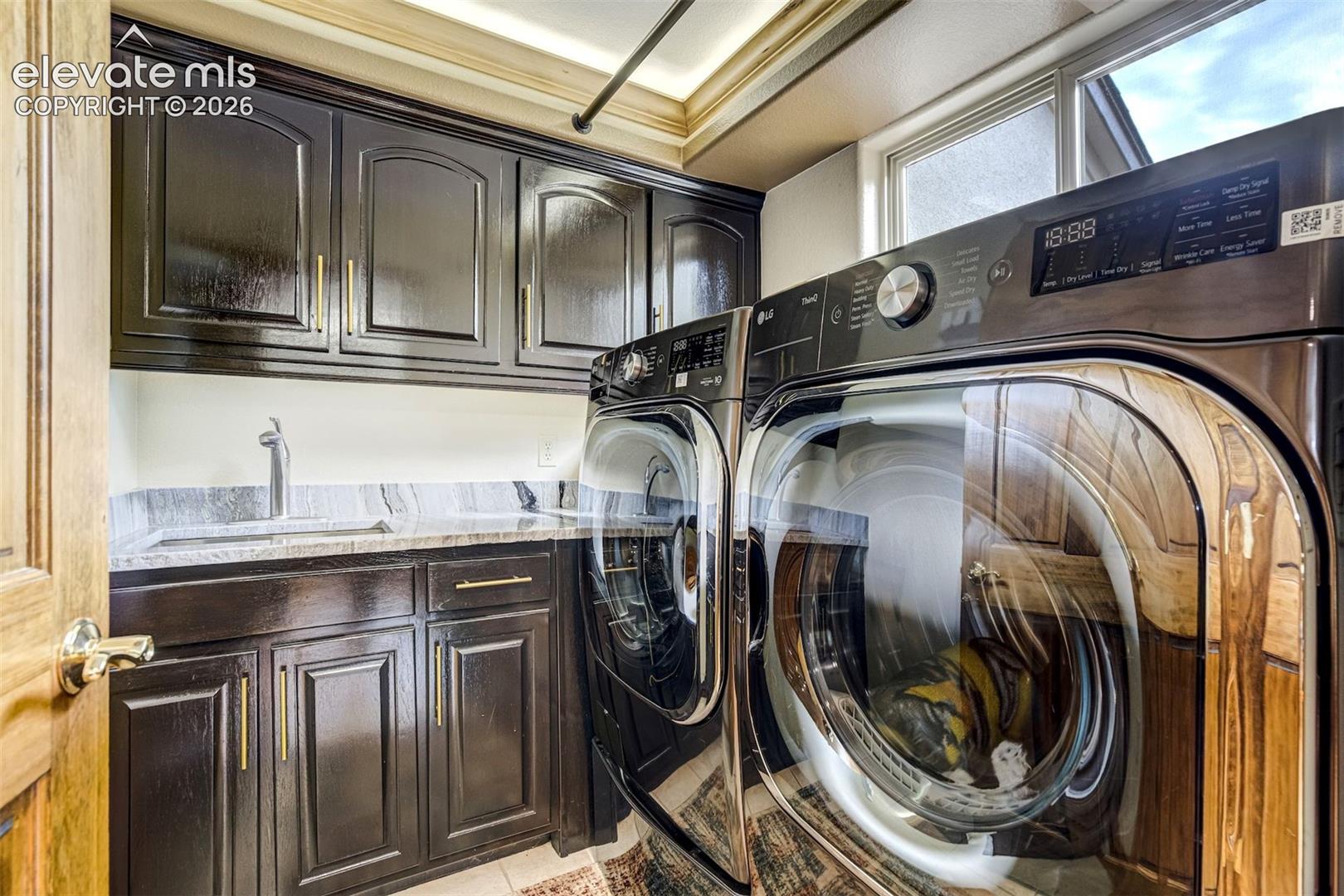 Laundry area featuring dark wood cabinetry, a built-in sink with a gooseneck faucet, light-toned countertop, and recessed ceiling lighting