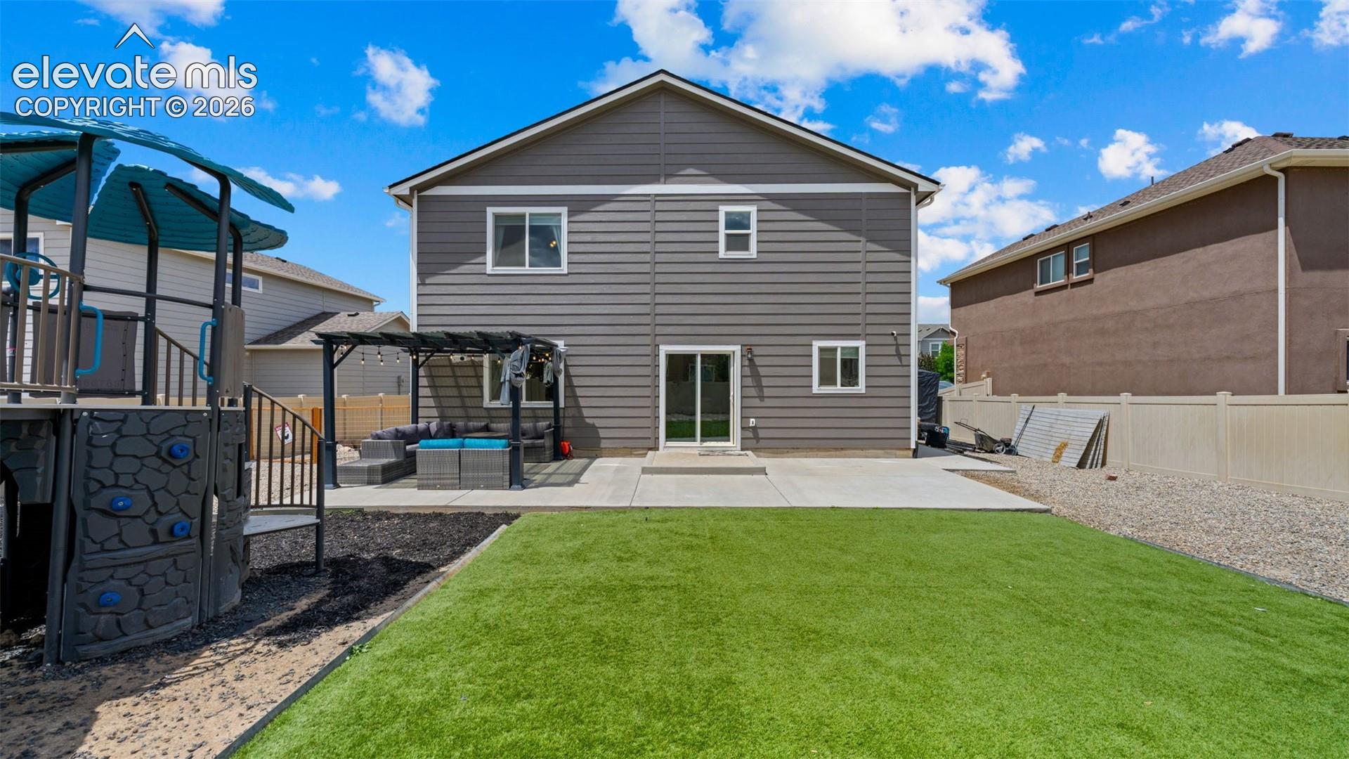 Rear exterior featuring gray siding, a concrete patio, and an artificial turf lawn