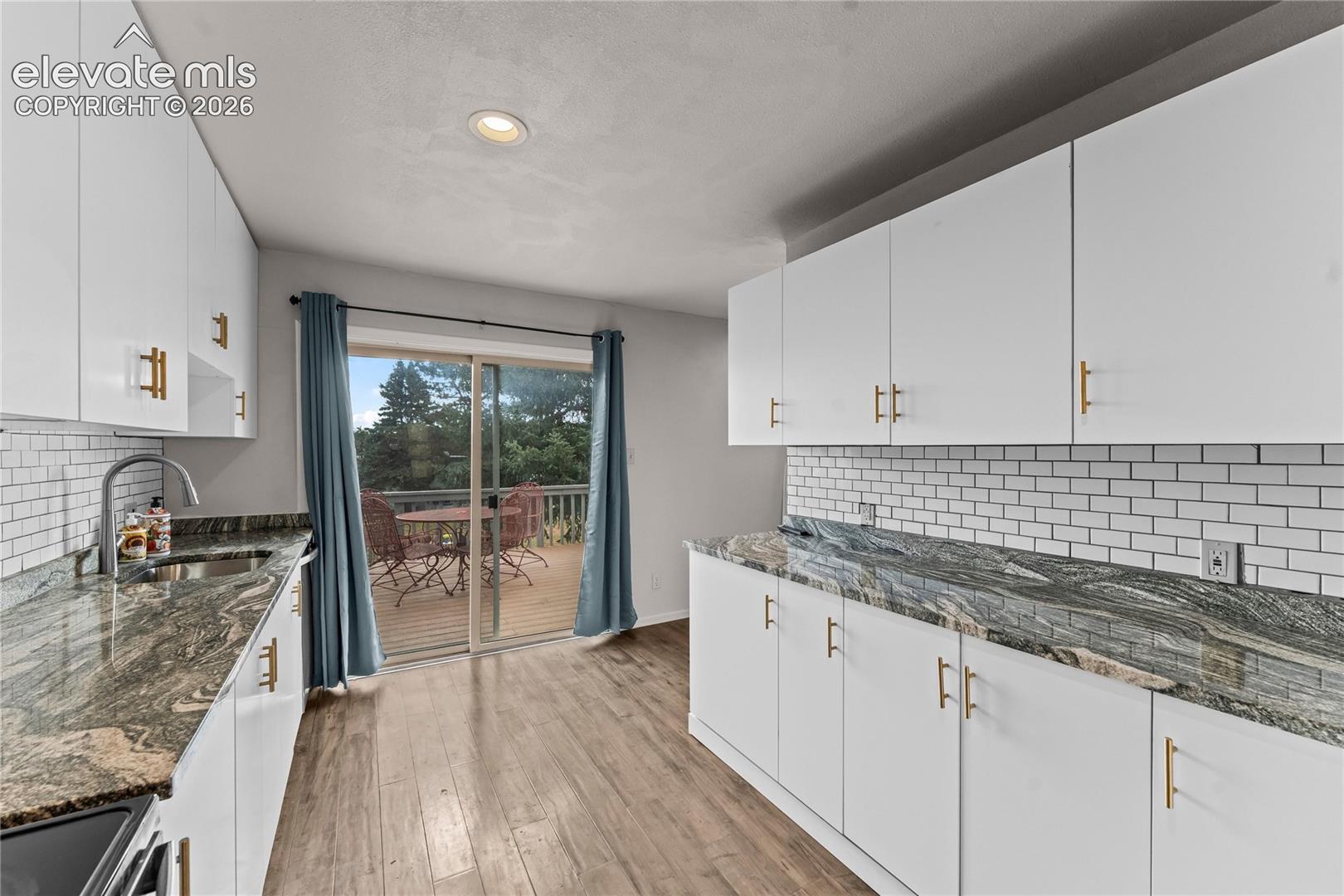 Kitchen featuring white cabinetry with gold-tone hardware, stone countertops, white subway tile backsplash, recessed lighting, and wood-finish flooring